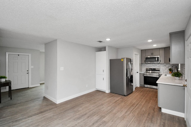 1030 San Felipe Rd, Sealy, TX 77474 - kitchen with stainless steel appliances, light countertops, light wood-type flooring, gray cabinets, and decorative backsplash
