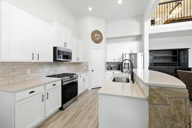 16413 Stonewall St, Conroe, TX 77303 - kitchen featuring appliances with stainless steel finishes, an island with sink, decorative backsplash, white cabinetry, and light wood-style floors