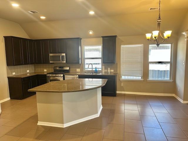 19522 Brighton Brook Ln, Richmond, TX 77407 - kitchen with stainless steel appliances, vaulted ceiling, tasteful backsplash, light tile patterned floors, and a chandelier