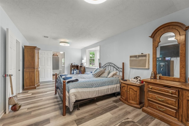 703 Pecan Valley Dr, Wharton, TX 77488 - bedroom featuring a textured ceiling, light wood-style flooring, and an AC wall unit