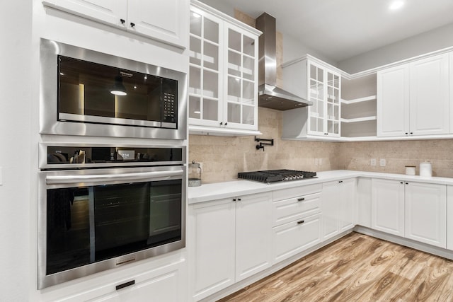 25203 Elijah Ct, Tomball, TX 77375 - kitchen with stainless steel appliances, wall chimney exhaust hood, light wood-style floors, light countertops, and white cabinets