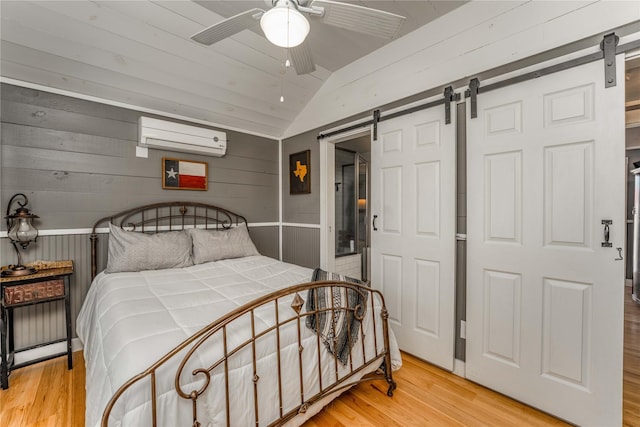 210 N Scott St, Fayetteville, TX 78940 - bedroom featuring a barn door, an AC wall unit, vaulted ceiling, light wood-style flooring, and wooden walls