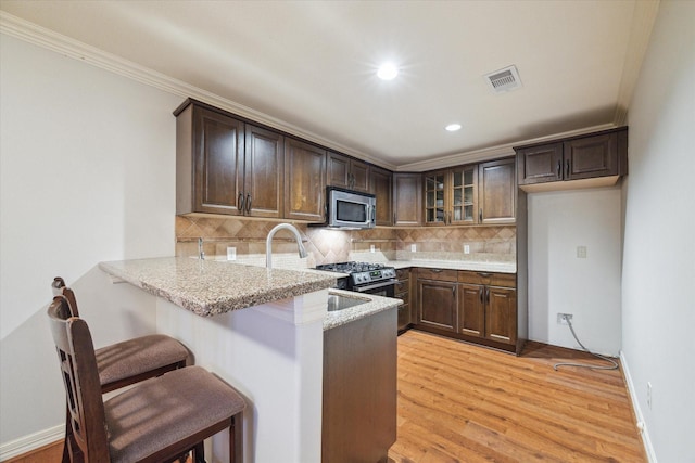 1002 Cowards Creek Ct, Friendswood, TX 77546 - kitchen with appliances with stainless steel finishes, a peninsula, glass insert cabinets, light stone countertops, and decorative backsplash