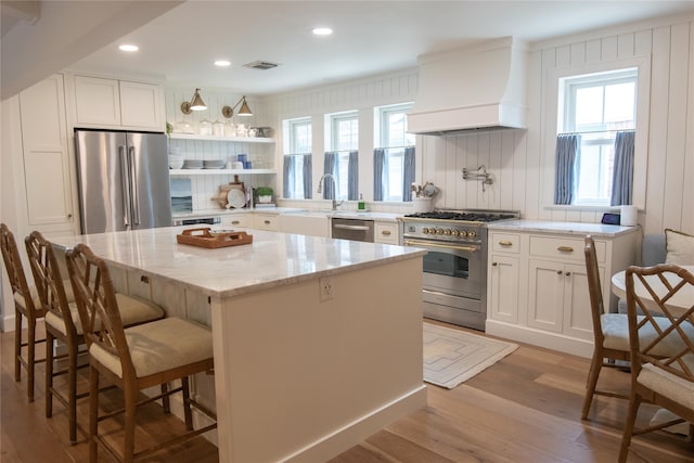 7611 Fairdale Ln, Houston, TX 77063 - kitchen featuring appliances with stainless steel finishes, premium range hood, light wood-style flooring, light stone countertops, and a center island