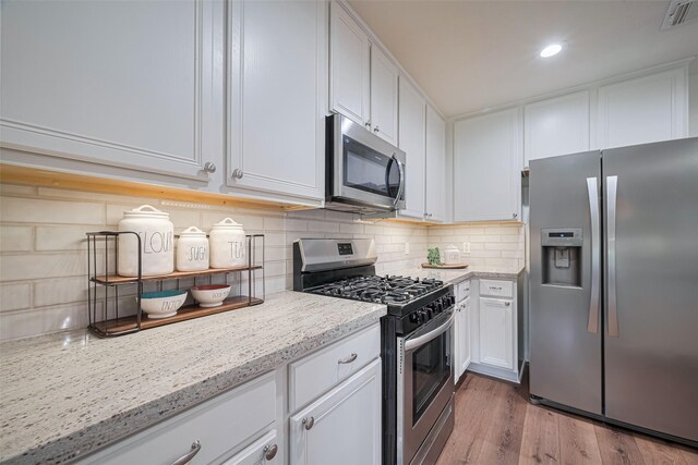 14311 Cally Cir, Needville, TX 77461 - kitchen featuring appliances with stainless steel finishes, tasteful backsplash, white cabinetry, wood finished floors, and recessed lighting