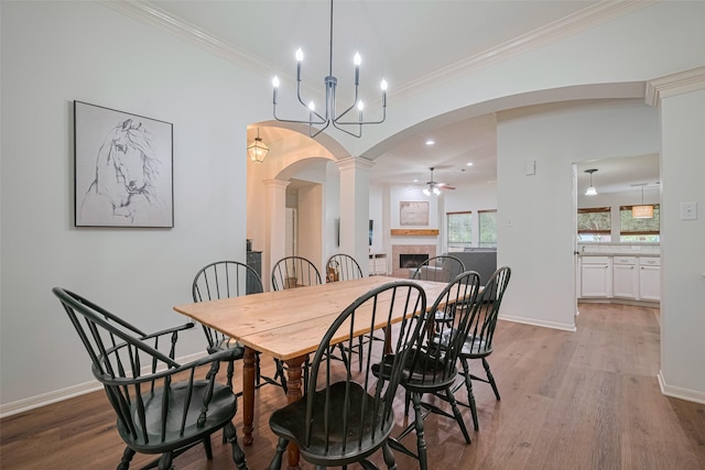 14311 Cally Cir, Needville, TX 77461 - dining space featuring light wood-style floors, arched walkways, a tiled fireplace, ceiling fan, and crown molding