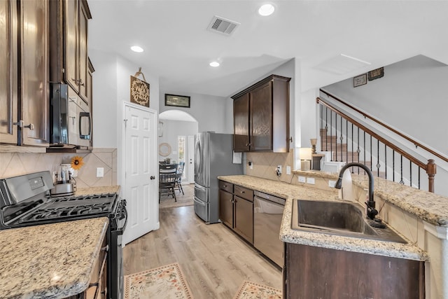 10211 Norway Spruce Ln, Tomball, TX 77375 - kitchen featuring appliances with stainless steel finishes, dark brown cabinetry, arched walkways, a peninsula, and light wood-style flooring