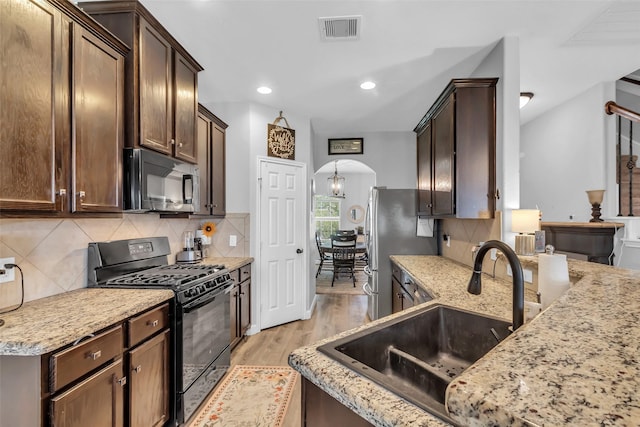 10211 Norway Spruce Ln, Tomball, TX 77375 - kitchen featuring black appliances, arched walkways, dark brown cabinetry, light wood-type flooring, and tasteful backsplash