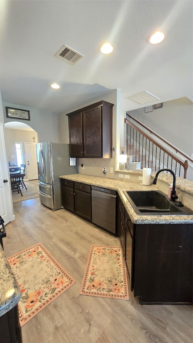 10211 Norway Spruce Ln, Tomball, TX 77375 - kitchen with stainless steel appliances, light wood-style floors, dark brown cabinets, arched walkways, and backsplash
