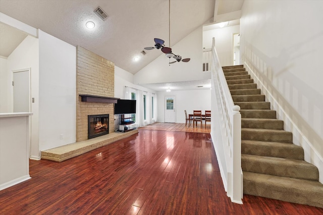 4790 Whispering Falls Dr, Houston, TX 77084 - unfurnished living room featuring ceiling fan, wood-type flooring, stairs, a fireplace, and high vaulted ceiling