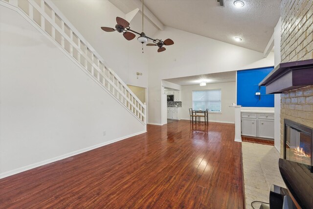 4790 Whispering Falls Dr, Houston, TX 77084 - unfurnished living room with a brick fireplace, a ceiling fan, stairway, wood finished floors, and high vaulted ceiling