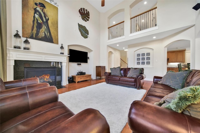 5714 Spring River Ln, Fulshear, TX 77441 - living room featuring wood finished floors, a towering ceiling, a tiled fireplace, and arched walkways