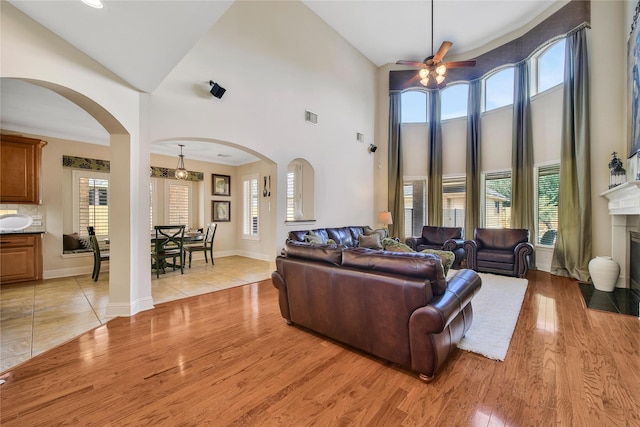 5714 Spring River Ln, Fulshear, TX 77441 - living area featuring arched walkways, ceiling fan, light wood-type flooring, a towering ceiling, and a fireplace with flush hearth