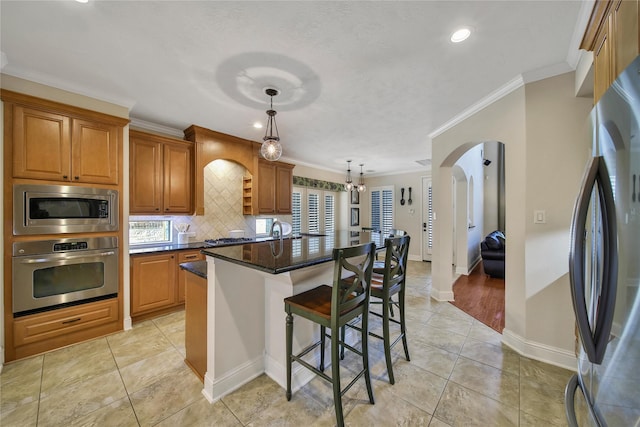 5714 Spring River Ln, Fulshear, TX 77441 - kitchen featuring appliances with stainless steel finishes, ornamental molding, brown cabinetry, tasteful backsplash, and a center island with sink