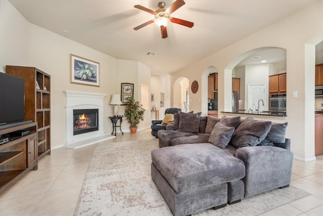 22911 Banff Brook Way, Tomball, TX 77375 - living room featuring light tile patterned floors, a ceiling fan, arched walkways, and a warm lit fireplace
