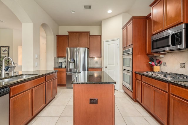 22911 Banff Brook Way, Tomball, TX 77375 - kitchen featuring appliances with stainless steel finishes, arched walkways, a center island, dark stone counters, and tasteful backsplash