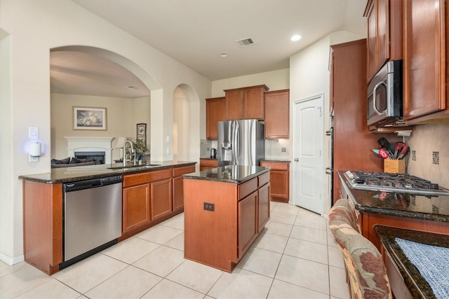 22911 Banff Brook Way, Tomball, TX 77375 - kitchen featuring appliances with stainless steel finishes, a kitchen island, brown cabinets, arched walkways, and dark stone countertops