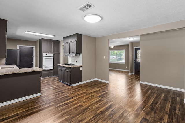 109 Timber Ln, Baytown, TX 77520 - kitchen with a warming drawer, appliances with stainless steel finishes, dark wood-style flooring, light stone counters, and backsplash