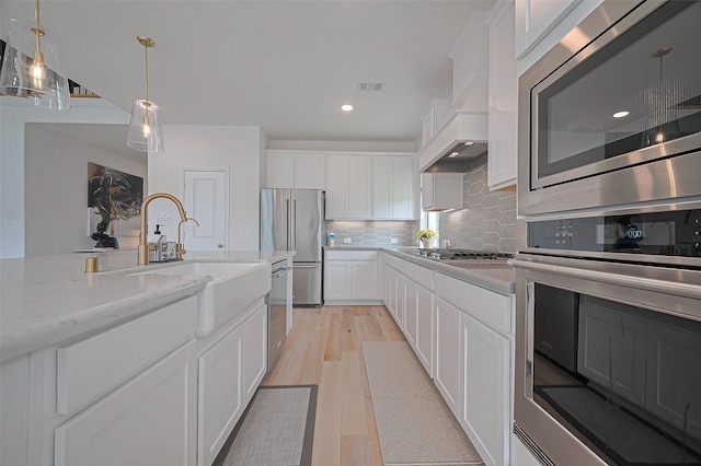 2611 Oakland Park Dr, Conroe, TX 77385 - kitchen with appliances with stainless steel finishes, light wood finished floors, decorative backsplash, decorative light fixtures, and white cabinets