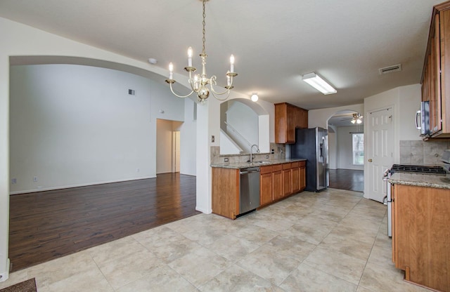 11610 Cross Spring Dr, Pearland, TX 77584 - kitchen with stainless steel appliances, decorative backsplash, arched walkways, and brown cabinets