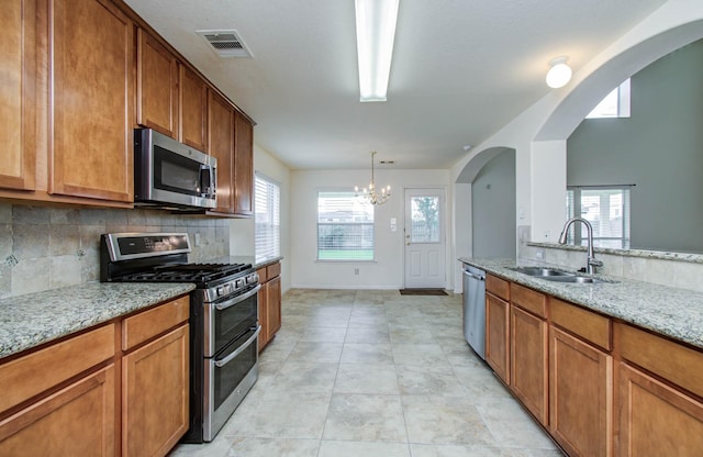 11610 Cross Spring Dr, Pearland, TX 77584 - kitchen featuring appliances with stainless steel finishes, arched walkways, tasteful backsplash, brown cabinets, and light stone countertops