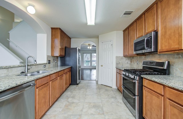 11610 Cross Spring Dr, Pearland, TX 77584 - kitchen with stainless steel appliances, light stone countertops, tasteful backsplash, brown cabinets, and arched walkways