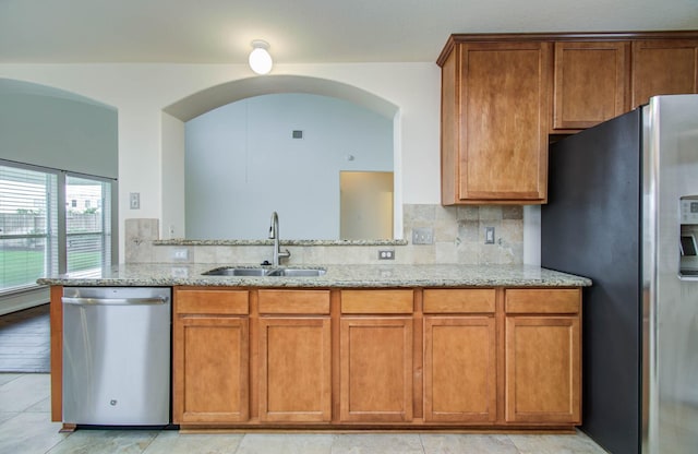 11610 Cross Spring Dr, Pearland, TX 77584 - kitchen featuring stainless steel appliances, brown cabinetry, light stone countertops, arched walkways, and decorative backsplash
