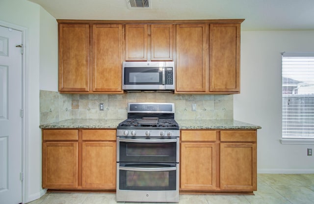 11610 Cross Spring Dr, Pearland, TX 77584 - kitchen featuring stainless steel appliances, light stone counters, decorative backsplash, and brown cabinetry