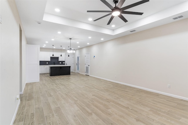 4120 S Kemp Ave, Edinburg, TX 78542 - unfurnished living room featuring a raised ceiling, recessed lighting, ceiling fan, light wood-type flooring, and a chandelier
