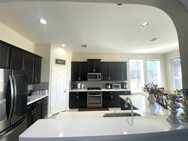 20718 Slate Ct, Richmond, TX 77407 - kitchen featuring appliances with stainless steel finishes, dark cabinets, tasteful backsplash, arched walkways, and recessed lighting