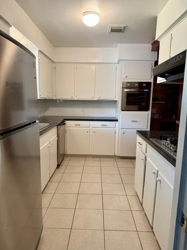 619 Rainy River Dr, Houston, TX 77037 - kitchen featuring appliances with stainless steel finishes, dark countertops, light tile patterned floors, and white cabinetry