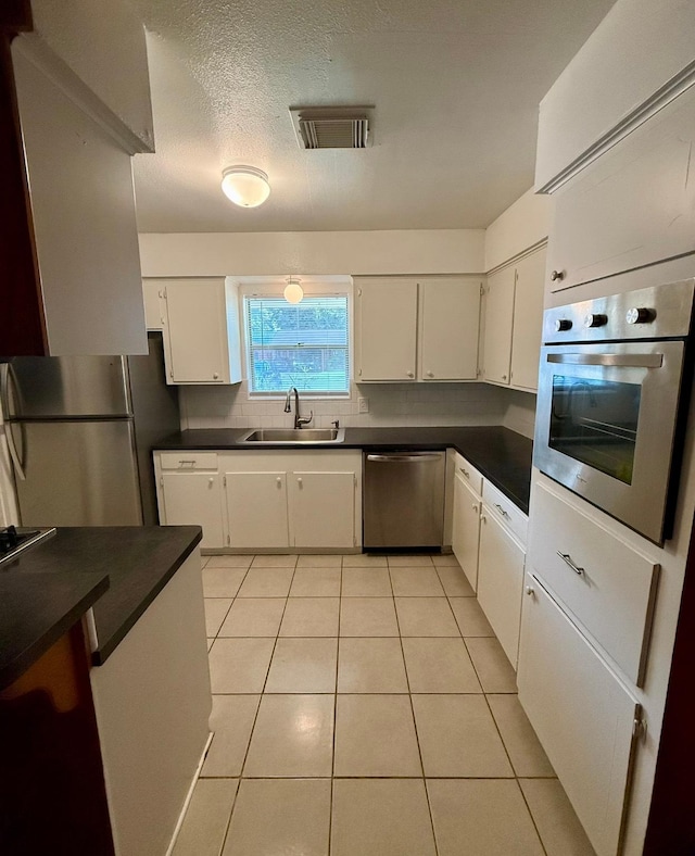 619 Rainy River Dr, Houston, TX 77037 - kitchen with stainless steel appliances, dark countertops, white cabinetry, light tile patterned flooring, and backsplash