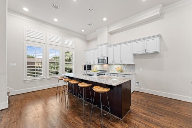 1705 Upland Lks, Houston, TX 77043 - kitchen featuring stainless steel microwave, crown molding, a kitchen breakfast bar, light stone countertops, and an island with sink