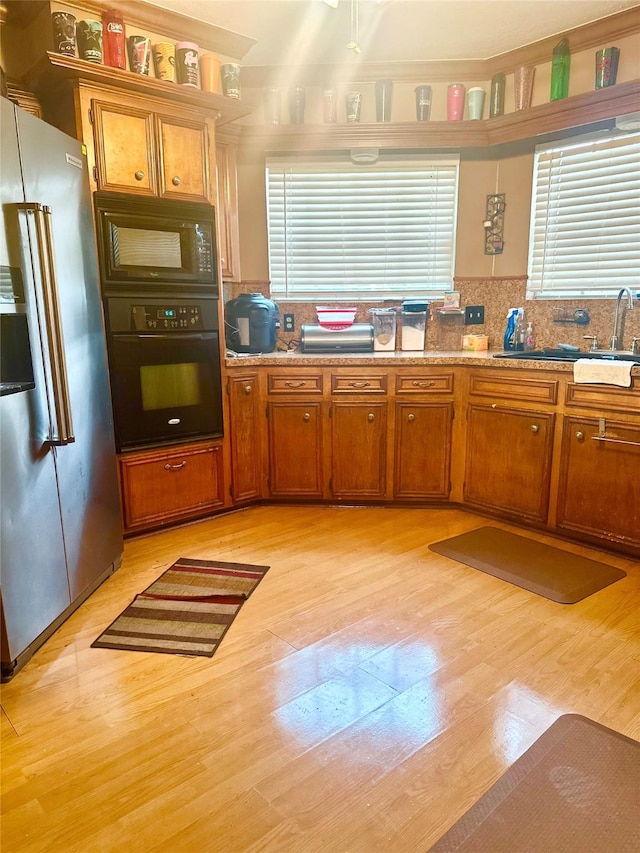 12006 Mill Trail Ln, Houston, TX 77070 - kitchen featuring black appliances, healthy amount of natural light, brown cabinets, and light wood-style floors