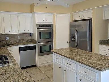 7822 Albin Ln, Houston, TX 77071 - kitchen featuring appliances with stainless steel finishes, white cabinetry, stone countertops, and a ceiling fan