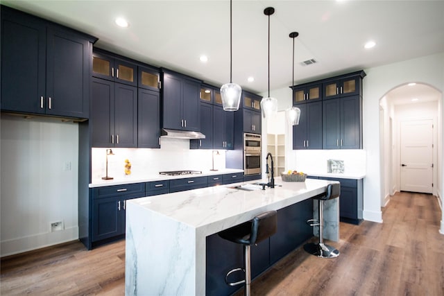 3314 Arbor St, Houston, TX 77004 - kitchen featuring wood finished floors, an island with sink, appliances with stainless steel finishes, arched walkways, and pendant lighting