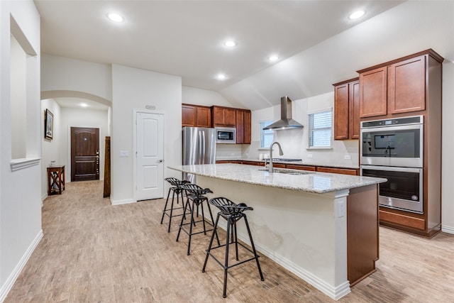 2821 Redbud Ln, Melissa, TX 75454 - kitchen featuring appliances with stainless steel finishes, wall chimney exhaust hood, a kitchen island with sink, light wood-style flooring, and lofted ceiling
