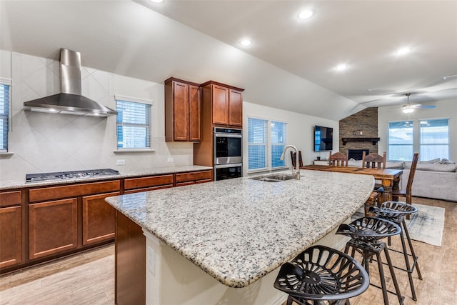 2821 Redbud Ln, Melissa, TX 75454 - kitchen with wall chimney exhaust hood, appliances with stainless steel finishes, ceiling fan, light wood-style floors, and vaulted ceiling