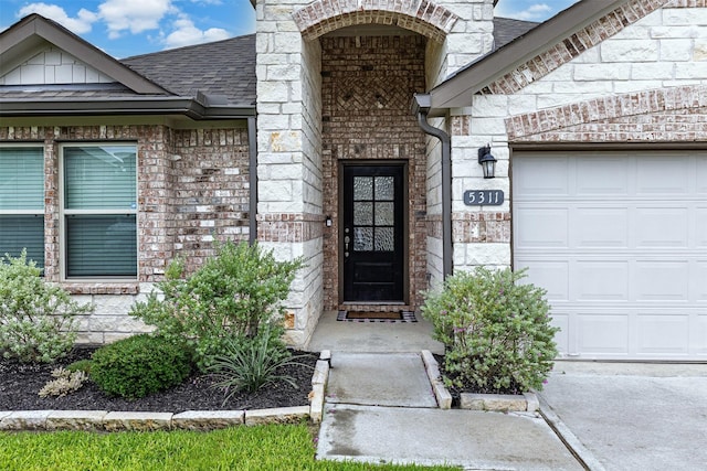 5311 Latigo Ct, Alvin, TX 77511 - view of exterior entry with stone siding, a shingled roof, an attached garage, and brick siding
