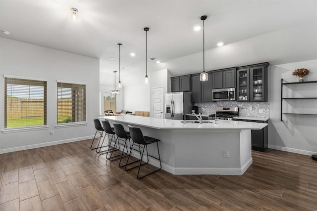 5311 Latigo Ct, Alvin, TX 77511 - kitchen featuring stainless steel appliances, a large island with sink, light countertops, decorative backsplash, and dark wood finished floors