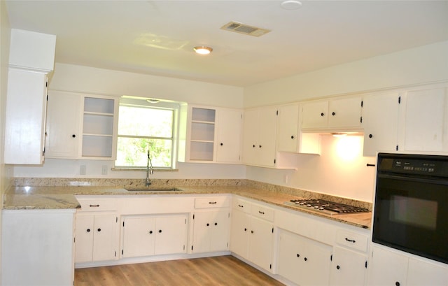 101 Summit Dr, Conroe, TX 77303 - kitchen featuring black oven, stainless steel gas stovetop, light stone counters, light wood-style floors, and white cabinets