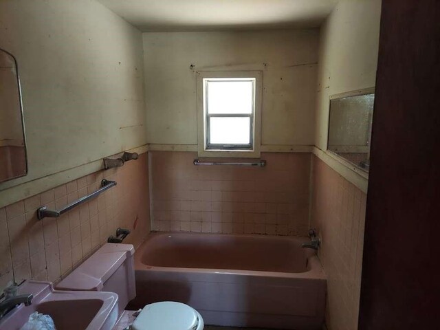 343 NW Martin Luther King Dr, De Kalb, TX 75559 - bathroom featuring tile walls, a bathtub, and a wainscoted wall