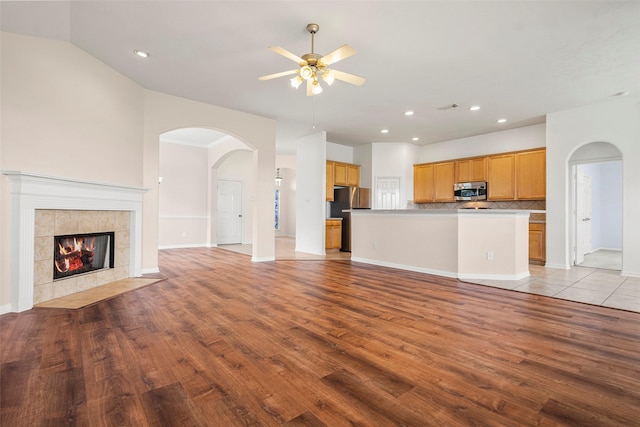 12610 Hobbs Terrace Dr, Tomball, TX 77377 - unfurnished living room featuring light wood finished floors, ceiling fan, arched walkways, recessed lighting, and a tile fireplace