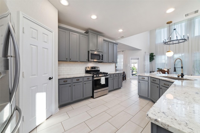 18534 Tall Woods Pl, Houston, TX 77084 - kitchen with stainless steel appliances, gray cabinetry, decorative backsplash, light stone countertops, and a chandelier