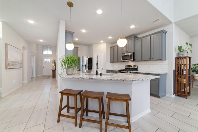 18534 Tall Woods Pl, Houston, TX 77084 - kitchen with stainless steel appliances, gray cabinets, tasteful backsplash, a kitchen bar, and light stone counters