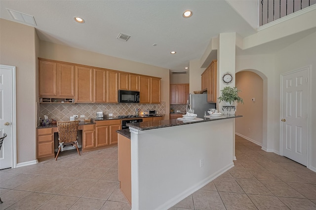 15902 Mill Canyon Ct, Cypress, TX 77429 - kitchen with black appliances, light tile patterned flooring, arched walkways, tasteful backsplash, and dark stone countertops