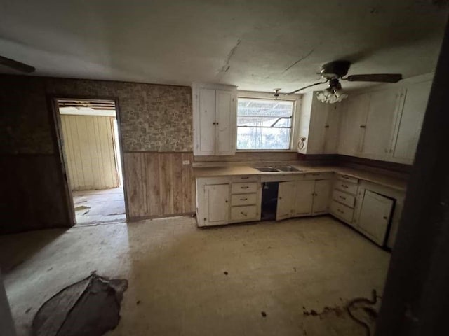 509 N Waggoner St, Electra, TX 76360 - kitchen featuring wainscoting, wooden walls, a ceiling fan, and white cabinets