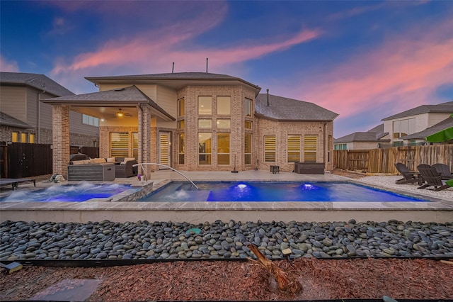 9011 Bright Harbor Dr, Cypress, TX 77433 - back of house at dusk featuring an in-ground hot tub, brick siding, a fenced backyard, and a patio area
