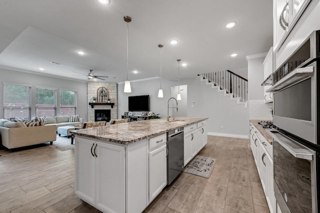 25119 Dunbrook Springs Ln, Katy, TX 77494 - kitchen featuring stainless steel appliances, ceiling fan, a fireplace, open floor plan, and an island with sink