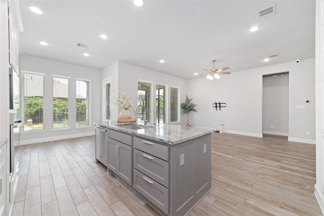 18402 Ingliston Ln, Richmond, TX 77407 - kitchen with gray cabinetry, ceiling fan, light wood finished floors, stainless steel appliances, and an island with sink